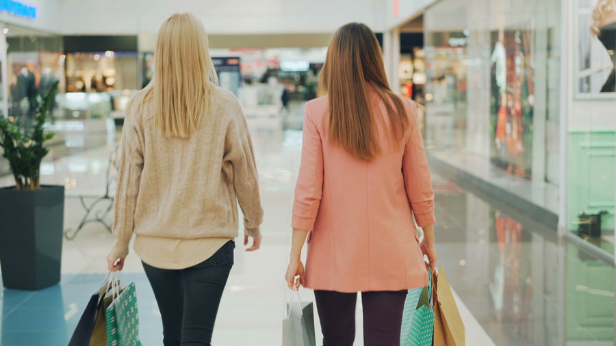 Two shoppers carry bags through a shopping mall.