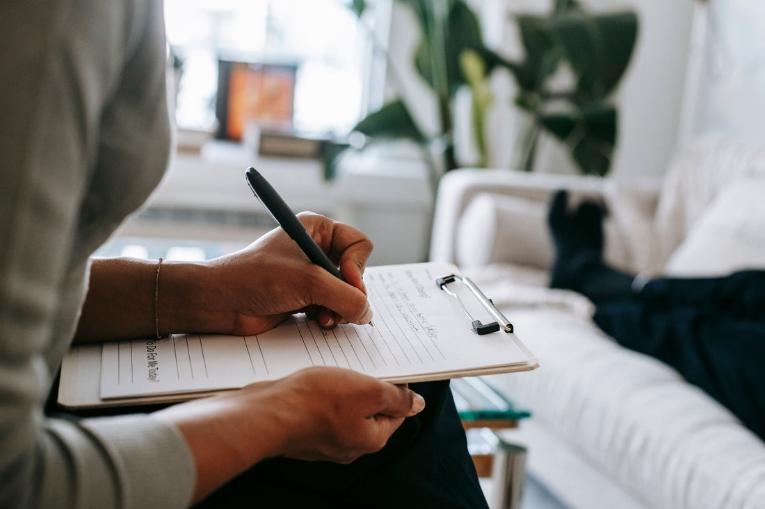 Person writing notes on a clipboard during a therapy or coaching session.