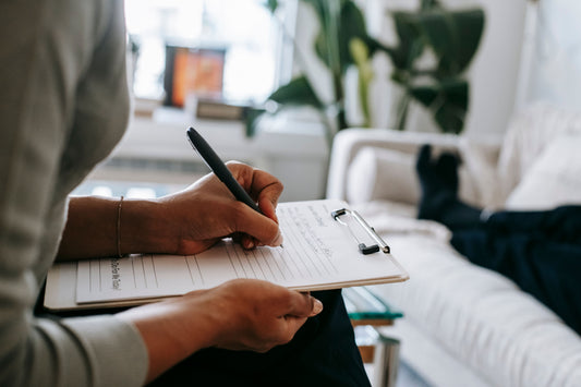 Person writing notes on a clipboard during a therapy or coaching session.