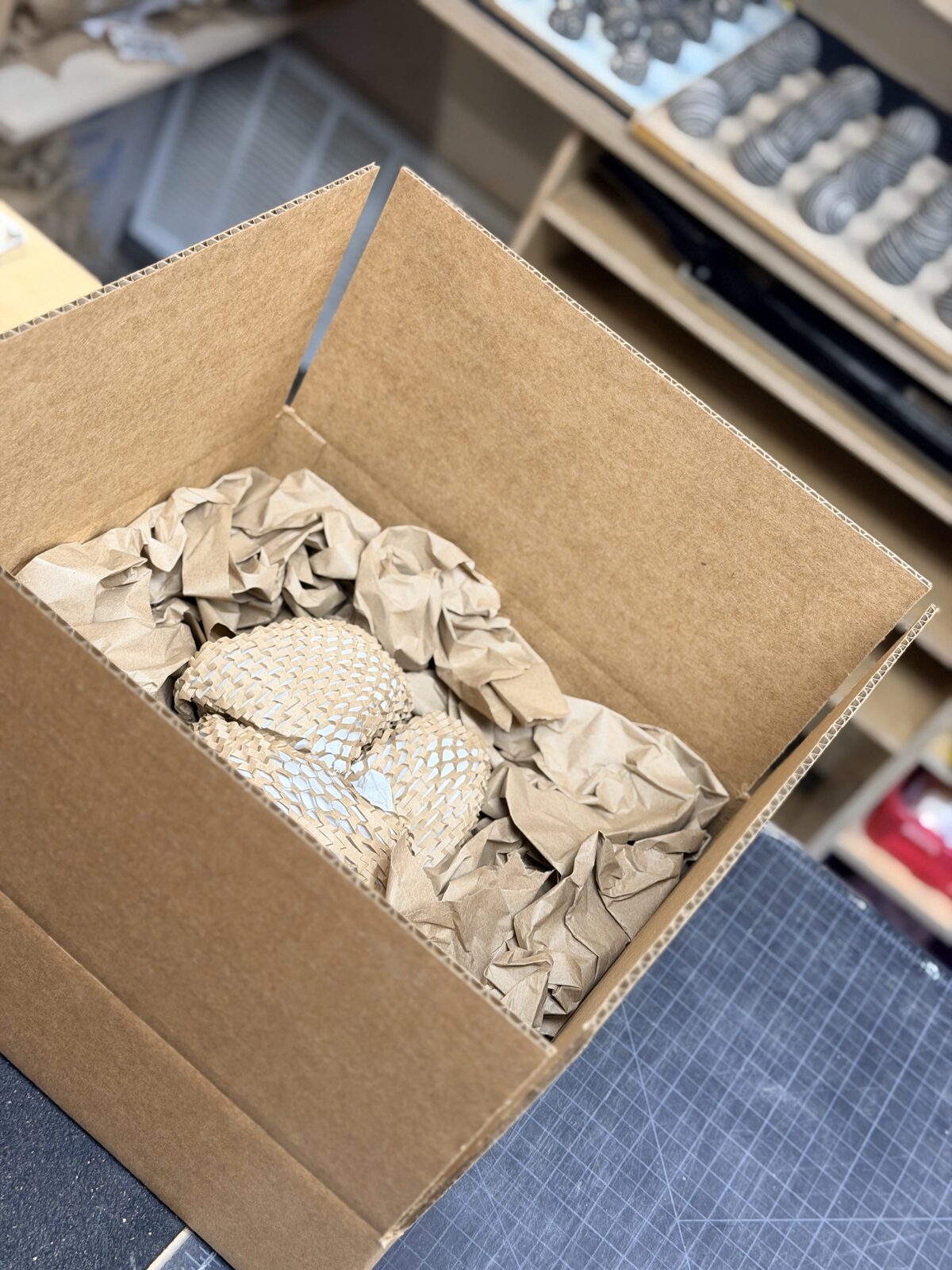 Two wrapped objects cushioned with crumpled paper in a cardboard box