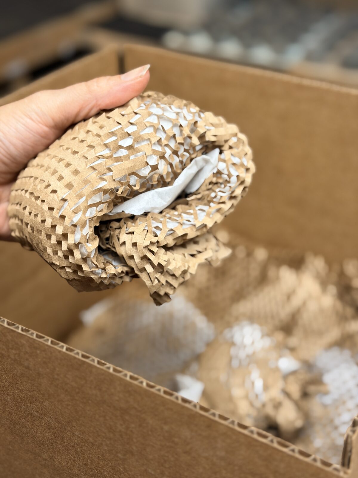 Hand holding honeycomb paper around an object above a cardboard box
