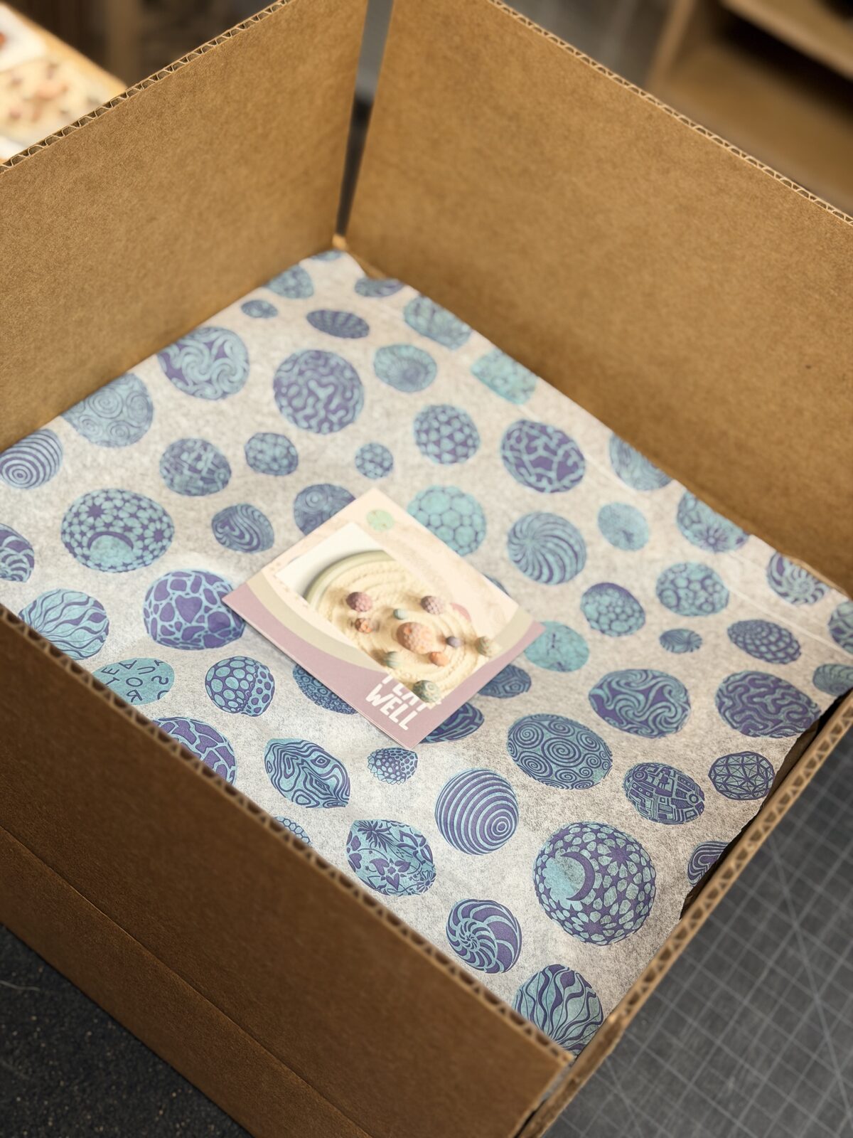 Printed sphere-pattern tissue and a Play Well card inside a cardboard box