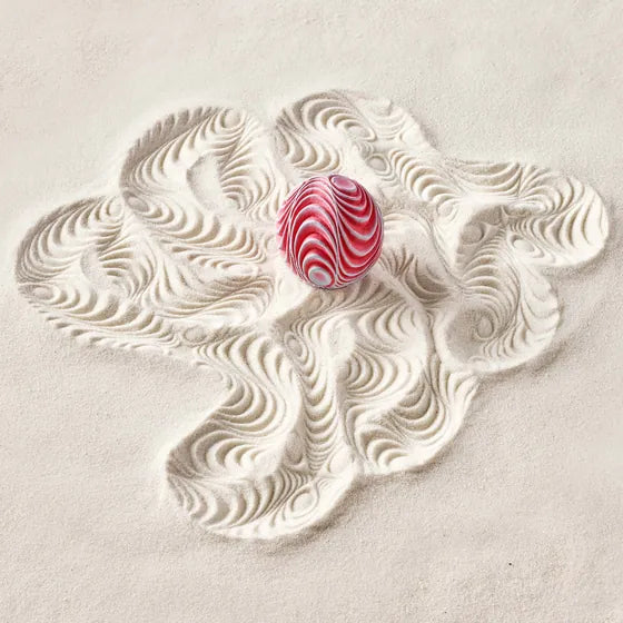 A red and blue Squiggle Sand Sphere on sand printed with wavy tracks.