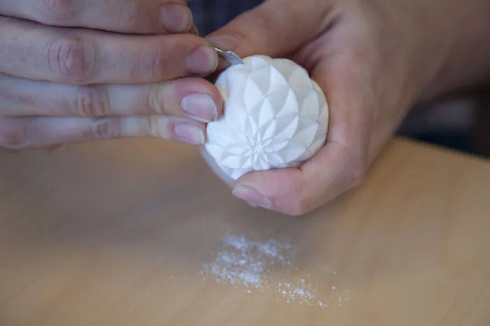 Andrew hand-carves a light-colored patterned original over a work table.