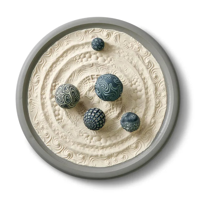 Wayfinder Wonderscape from above: a large gray round tray of patterned sand with five blue and slate spheres.