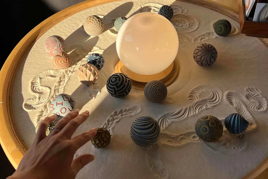 Hands roll Sand Spheres through a large tray of sand at Olander's Portland Saturday Market booth.