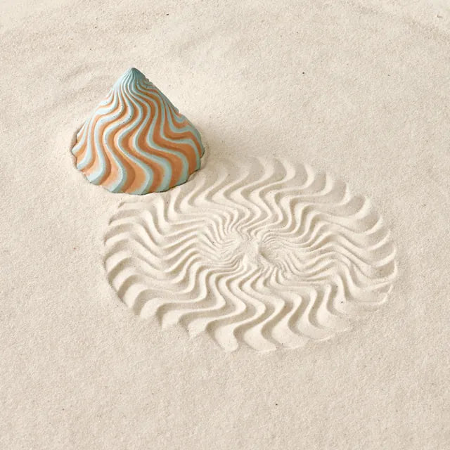 A striped Groovy Sand Cone standing in sand beside the pattern it left.