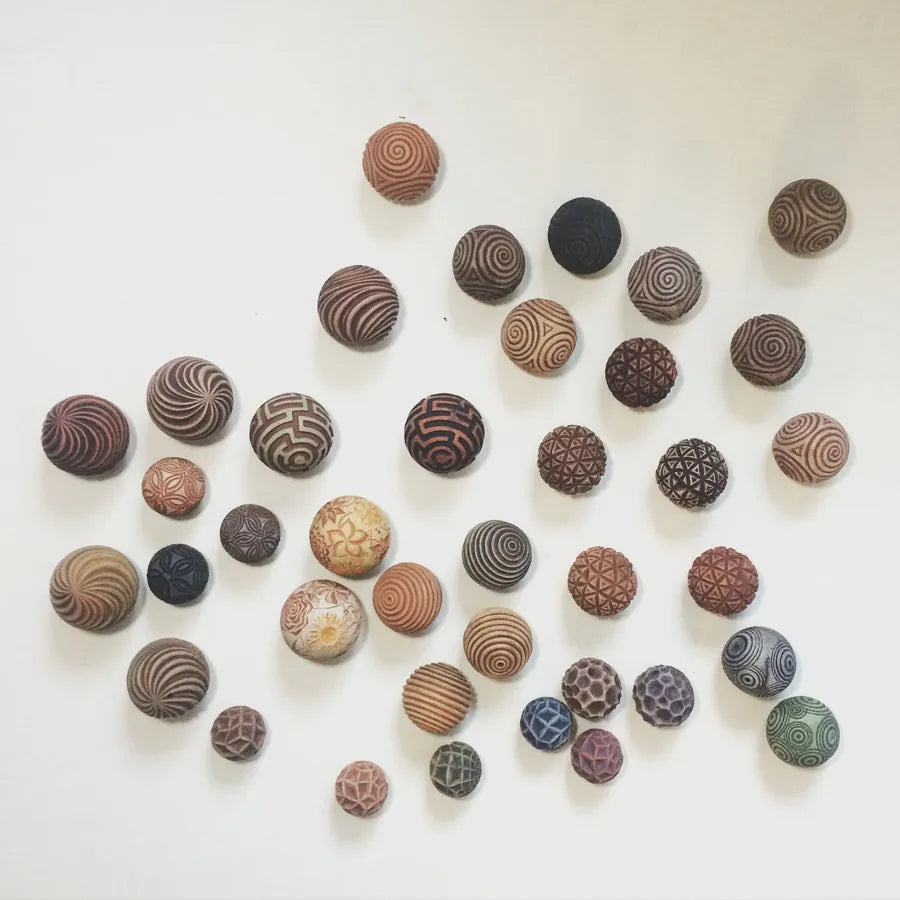 Dozens of patterned Sand Spheres in earthy colors scattered across a white surface.