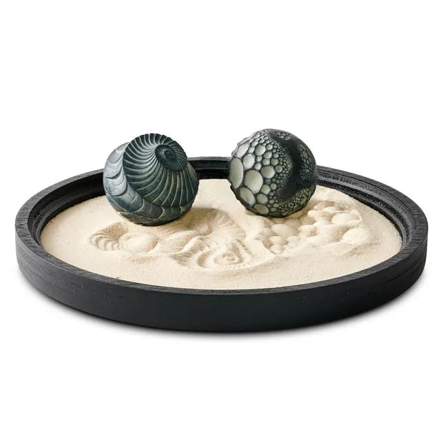 A dark tray of sand with two patterned forms.