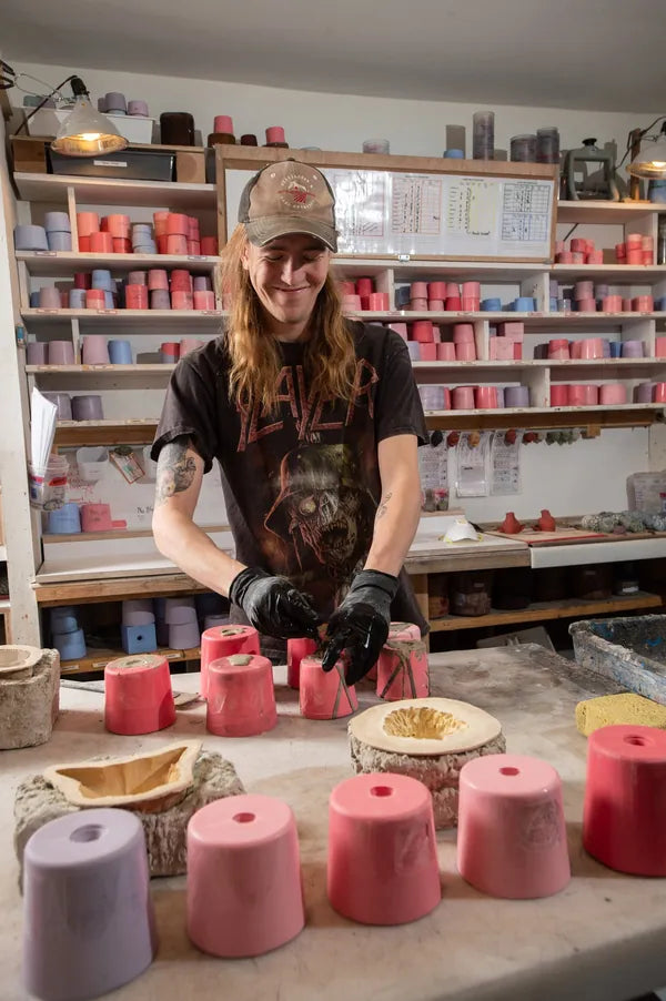 A studio team member in gloves works at a table lined with pink molds.