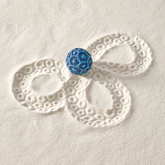 A blue Coral Sand Sphere beside the looping pattern it rolled in sand.
