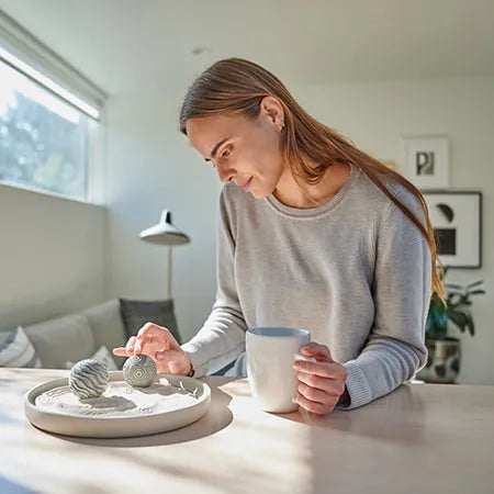 A person with a mug rolls a Sand Sphere in a Wonderscape at a kitchen table.