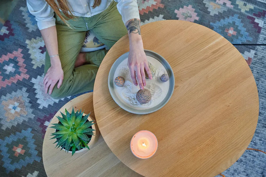 Seen from above, a person reaches into a small Wonderscape tray on a round side table, beside a succulent and a lit candle.
