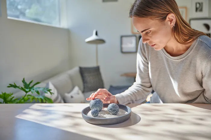 A woman rolls a Sand Sphere in a gray tray on a table in a bright living room.